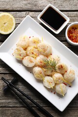 Raw scallops with spices, dill, lemon zest and sauces on wooden table, flat lay