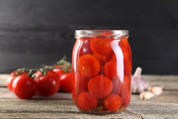 Tasty pickled tomatoes in jar, fresh vegetables and garlic on wooden table