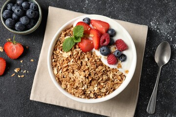Tasty granola with berries and yogurt served on dark textured table, flat lay