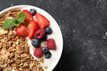 Tasty granola with berries and yogurt in bowl on dark textured table, top view. Space for text