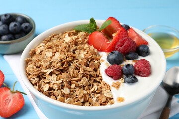 Tasty granola with berries and yogurt in bowl on light blue table, closeup