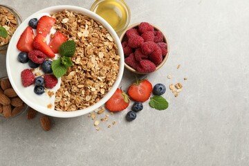 Tasty granola with berries and yogurt in bowl on grey textured table, flat lay. Space for text