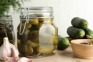 Pickled cucumbers in jars, peppercorns and garlic on wooden table, closeup
