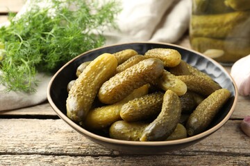Pickled cucumbers in bowl on wooden table, closeup