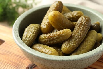 Pickled cucumbers in bowl on wooden board, closeup