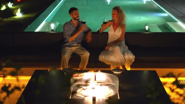 A couple basks in the glow of night by the poolside, enjoying a moment together with wine - Powered by Adobe