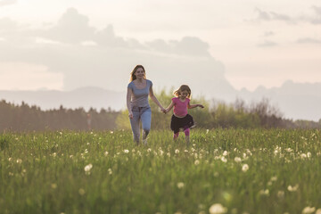 Fototapeta premium Mother and her little daughter running holding hands in the beautiful nature towards the setting sun.