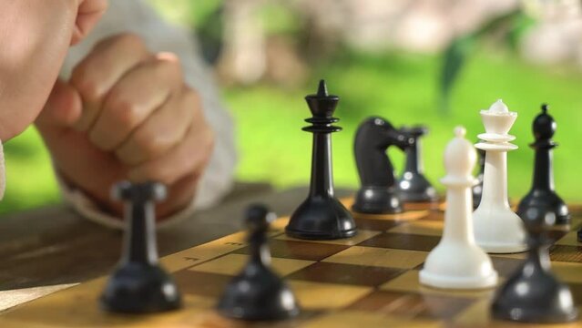 A young adult woman playing chess in the garden of her house or in summer park