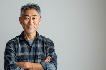Obraz premium Portrait of a merry asian man in his 50s with arms crossed isolated on minimalist or empty room background
