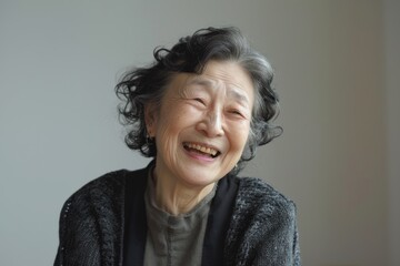 Portrait of a content asian woman in her 70s laughing on minimalist or empty room background