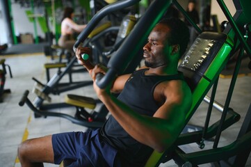 Fototapeta premium Athletic young black man having workout on chest press machine in gym