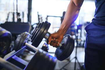 Close-up man grabs a heavy dumbbell in gym with his hand. Concept lifting, fitness