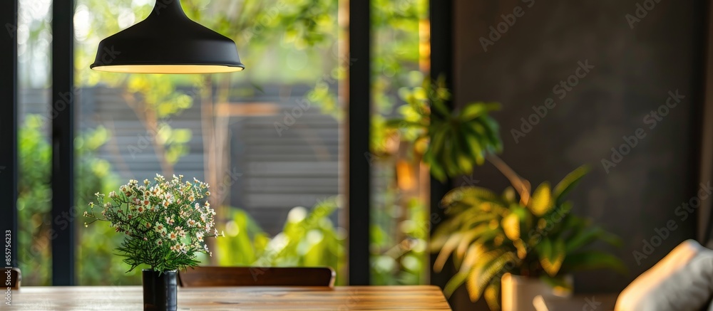 Poster wooden table with vase of flowers under black pendant lamp in modern living room with sofa near wind