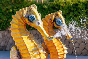 Detail from an aqua park in a hot summer day. Decorative sprinklers shaped like seahorse by the pool.  © Myst