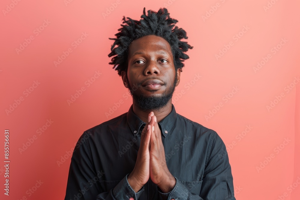 Wall mural Portrait of a tender afro-american man in his 30s joining palms in a gesture of gratitude in front of solid color backdrop - Wall murals
