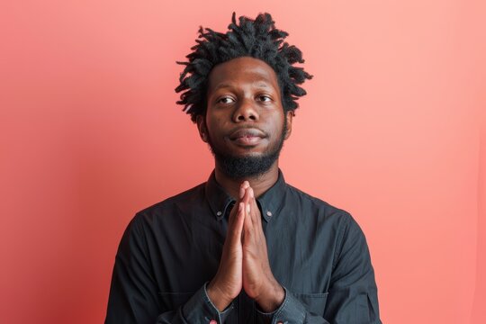 Portrait of a tender afro-american man in his 30s joining palms in a gesture of gratitude in front of solid color backdrop