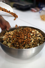 manos de persona echando almendras y frutos secos en una fuente para hacer un coctel de frutos secos