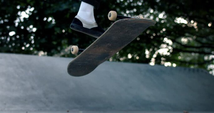 Super slow motion close up of determined and motivated skateboarder make ollie trick with skateboard at skate park ramp in urban city center at 1000 fps.
