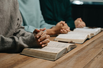 Group of Christians sit together and pray around a wooden table with blurred open Bible pages in their homeroom. Prayer for brothers, faith, hope, a