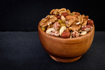 Mixed nuts in wooden bowl on black background.