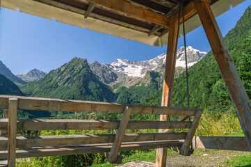 Wooden swing with a canopy to protect from the sun and rain in the mountains for relaxation. Vacation in the mountains in summer. Swing on the background of snow-capped mountain peaks in summer.