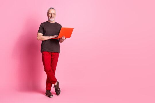 Full size photo of nice man with beard dressed t-shirt in glasses hold laptop stand near empty space isolated on pink color background