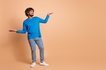 Photo of cheerful glad guy wear stylish blue clothes hold empty space look offer isolated on beige...