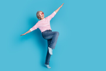 Full size photo of attractive retired woman heart sunglass playful flying dressed stylish striped clothes isolated on blue color background