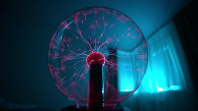 Closeup of toy plasma globe glowing in blurred background in dark room. Close-up of electric elegance of plasma ball illuminated by stormy lightning effects, slow motion. Concept of electric power.