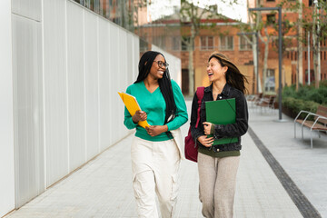 Two happy students girls talking and walking in University campus after classes