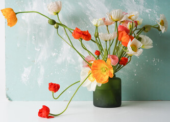 green vase with a mono bouquet of multi-colored poppies on a blue background