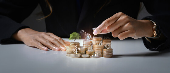 Businessman putting coin on stack with growing small tree symbolizing investment growth and saving...
