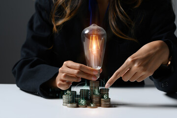 Businesswoman holding glowing light bulb over stack of coins with virtual icons. Business Innovation ideas concept