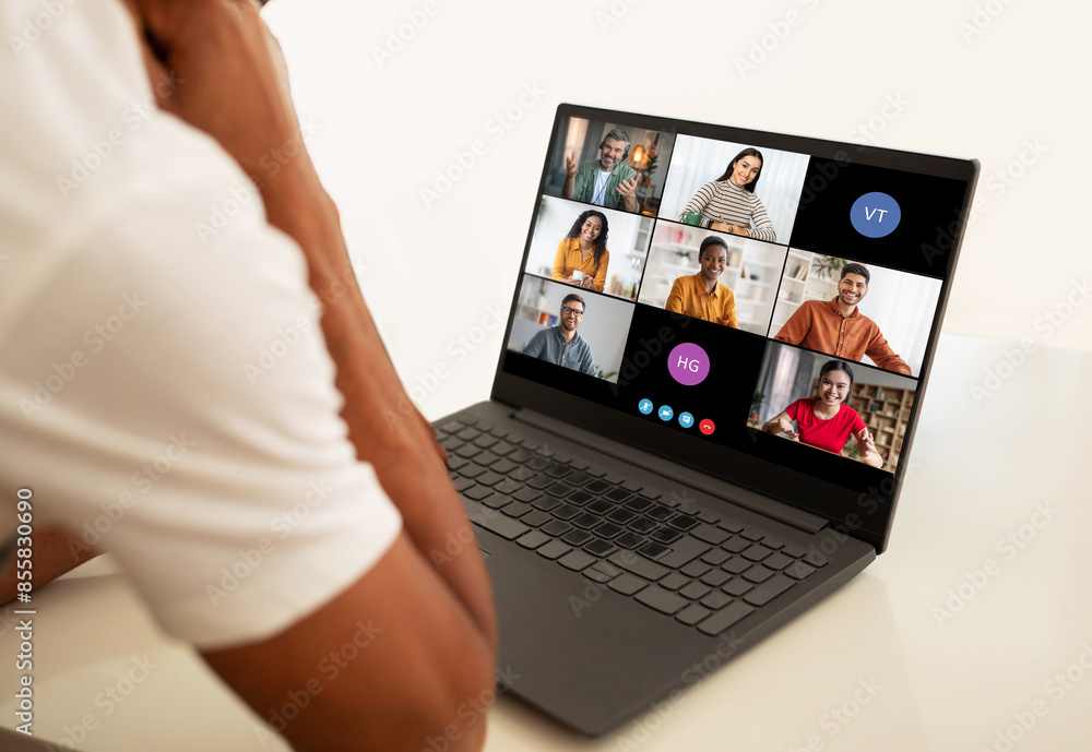 Poster a man sits at a desk, looking intently at his laptop screen. he is participating in a video conferen