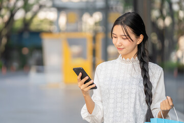 Fototapeta premium Asian woman in modern dress holding shopping bags walking outside a shopping mall.
