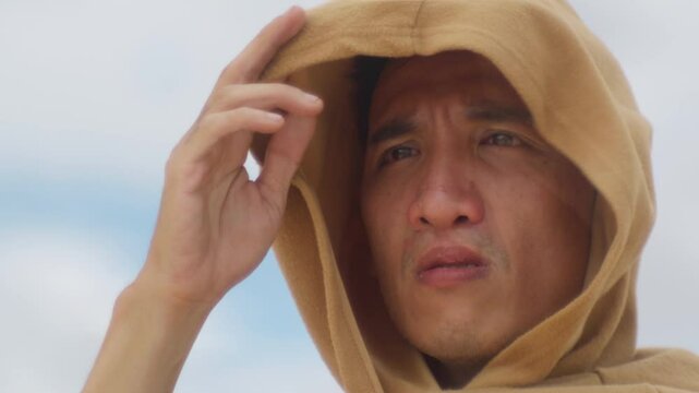 close up of a male chinese asiatic wearing a robe hood looking at the distance with a worried gaze during a wind storm