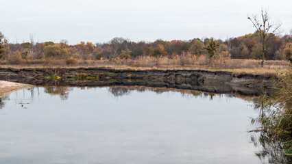 Siverskyi Donets river shore in Ukraine with autumn nature and grey sky reflections