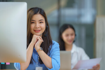 Happy smiling operator Asian woman customer service agent with headsets working on a computer in a call center.