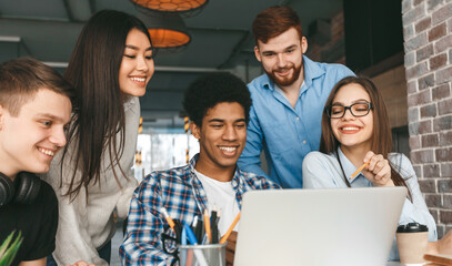 A group of five multiethnic students is gathered around a laptop, engaged in a collaborative effort. Their expressions are focused yet cheerful, suggesting they are working on a project they enjoy