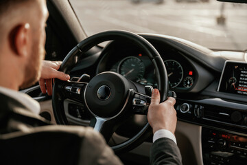Close up view of steering wheel. Man in black suit is sitting in the car, driving