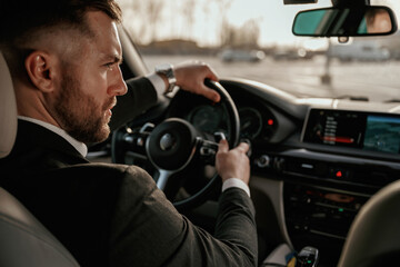 Driving, focused. Man in black suit is sitting in the car, driving