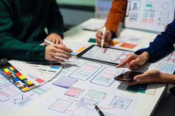 UX developer and ui designer brainstorming about mobile app interface wireframe design with customer breif and color code at office.