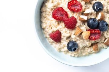 Oatmeal porridge with raspberries, blueberries and almonds in bowl isolated on white background
