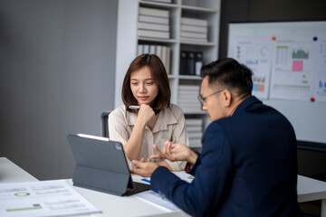 Fototapeta premium Two people are sitting at a desk with a laptop and a whiteboard
