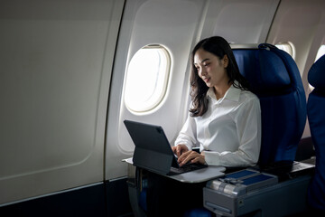 A woman is sitting on an airplane and using a laptop