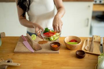 A woman is preparing a salad on a wooden table