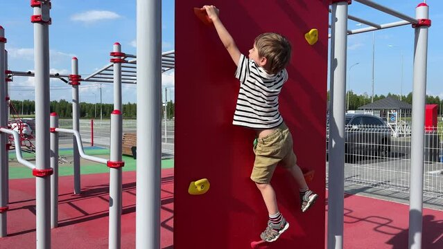 Strong and brave child boy is engaged in rock climbing on a street climbing wall. Toddler leisure activity