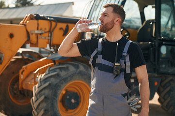 Bottle of water, drinking, taking a break. Man is with tractor. Agricultural worker