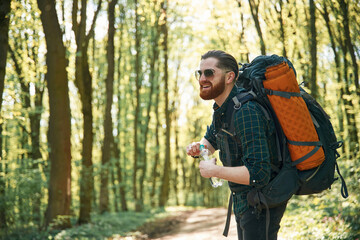 In glasses and with backpack. Bearded man is in the forest at daytime