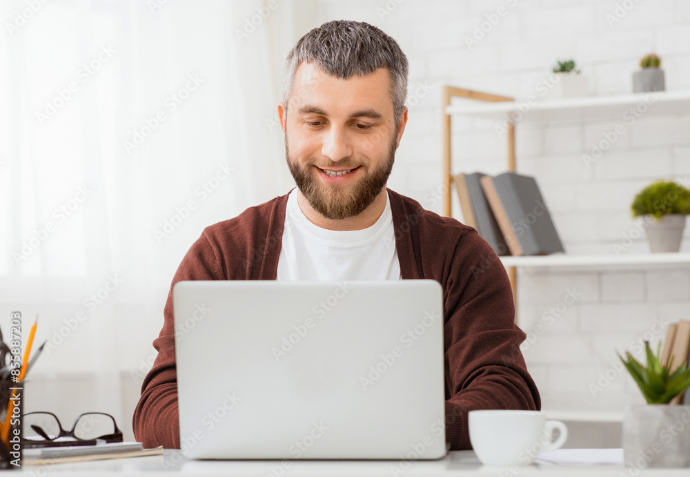 Aufkleber A man is seated in front of a laptop computer, focusing on the screen and typing on the keyboard. He appears engaged and concentrated on the digital tasks at hand.